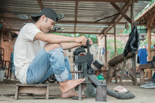 Reparador de neumáticos sostiene la prensa tradicional con sus pies mientras parchea neumáticos — Foto de Stock