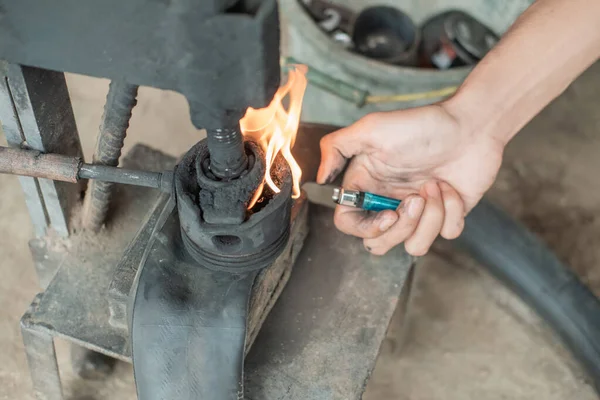 Primer plano de reparación de neumáticos mano al iniciar un fuego con un encendedor en una prensa tradicional —  Fotos de Stock