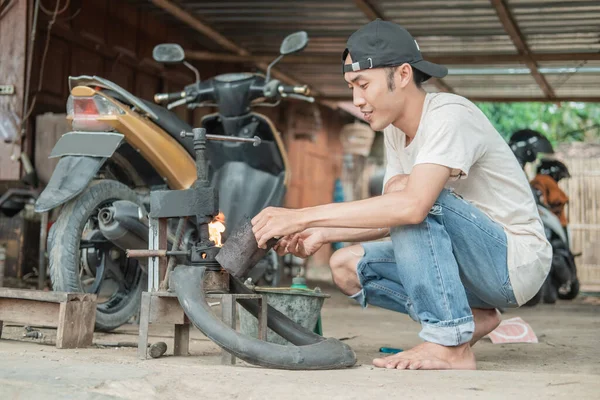 Réparateur de pneus allume un feu avec un briquet sur une presse traditionnelle tout en patcher un pneu de moto — Photo