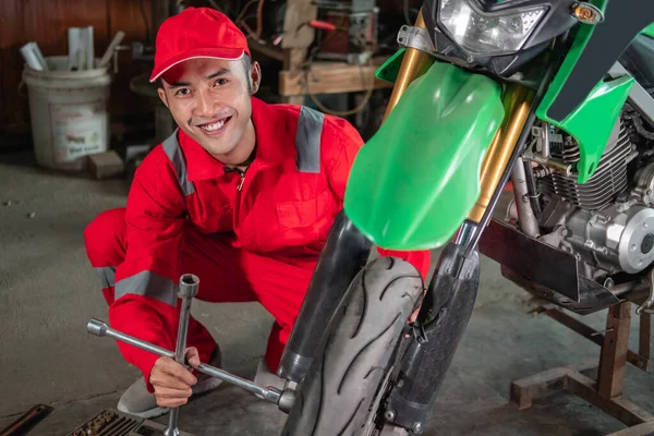 Mecánico sonríe a la cámara mientras usa las tuercas de las ruedas para quitar las ruedas de las motos —  Fotos de Stock