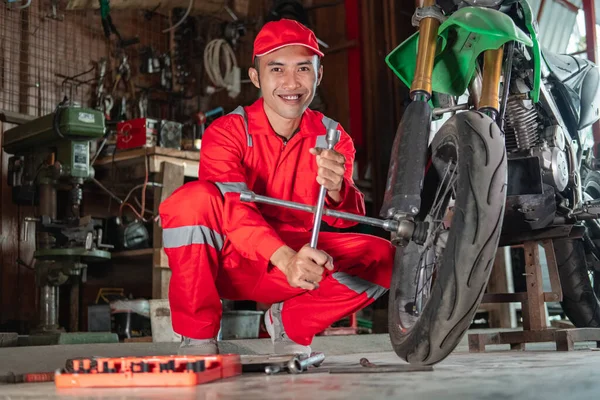 Side view of mechanic smiles at the camera while using wheel nuts to remove a motorcycle wheel — Stock Photo, Image