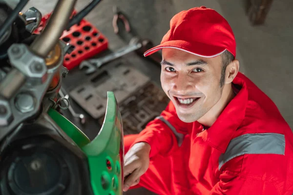 Un mécanicien souriant portant un chapeau à côté d'une moto — Photo