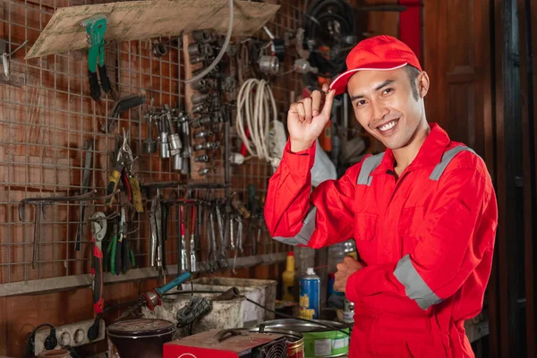 Uśmiechnięty mechanik w mundurze wearpack z kapeluszem stojącym w garażu — Zdjęcie stockowe
