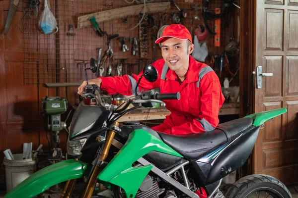 Pose of young mechanic in wearpack uniform and hat standing beside a dirt bike — Stock Photo, Image