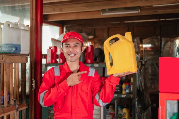 Pose av ung mekaniker i slitstark uniform och hatt stående med finger pekar medan du bär oljeflaska — Stockfoto