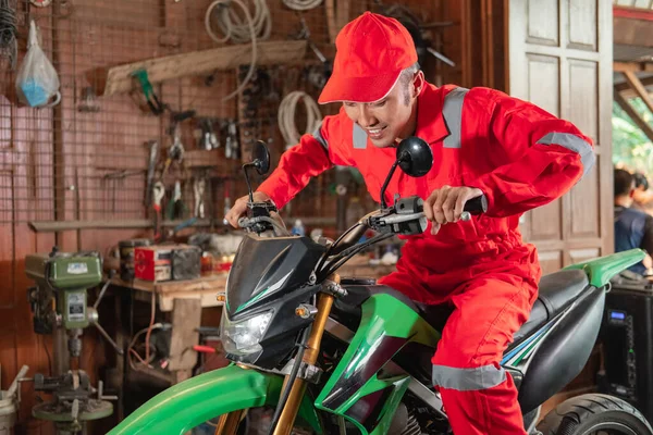 Pose of a mechanic wearing a wearpack and a hat riding a motorcycle while trying to brake a dirt bike — Stock Photo, Image
