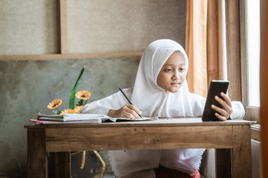 Endonezyalı liseli kız çevrimiçi dersi sırasında ödev çalışıyor.