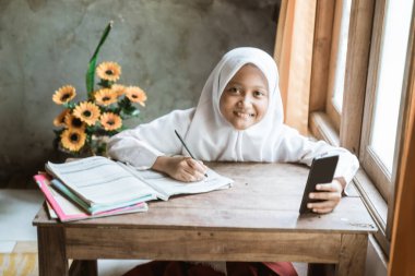 Endonezyalı liseli kız çevrimiçi dersi sırasında ödev çalışıyor.
