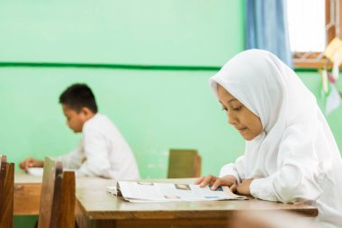 a portrait of an indonesian primary school student reading a textbook