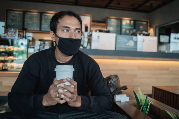 Man wachtend in een café onder het genot van koffie met gezichtsmasker — Stockfoto