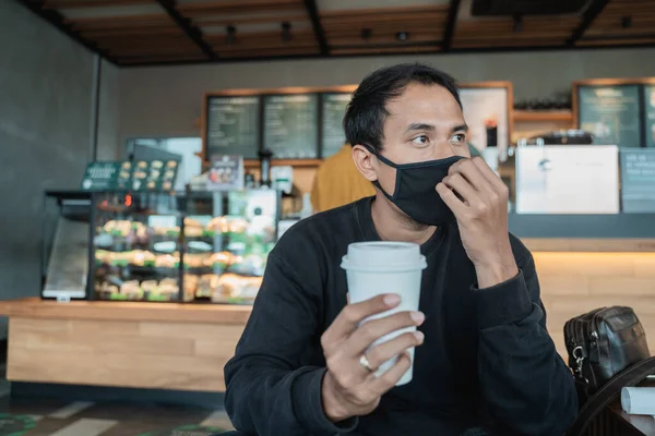 Homem esperando em um café enquanto desfruta de café com máscara facial — Fotografia de Stock