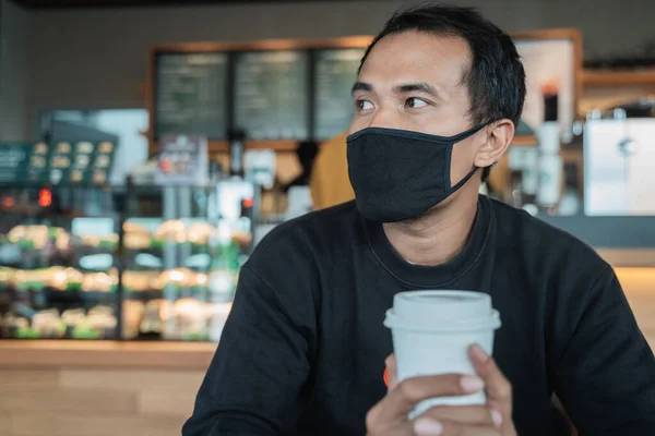 Hombre esperando en un café mientras disfruta del café con mascarilla — Foto de Stock