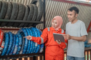 Peçeli, parmakla işaret eden üniformalı bir kadın tüketicilere raftaki lastiğin tipini gösteriyor.