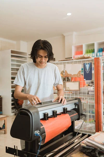 Genç erkek girişimci makine ile çıkartma kağıdı yapıyor. — Stok fotoğraf
