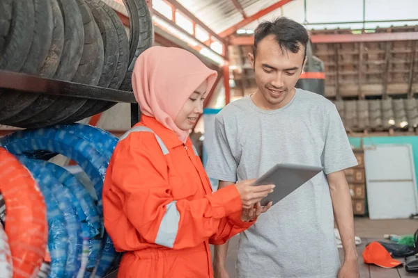 Mujeres hijab que usan uniformes de wearpack utilizan tabletas digitales para mostrar el tipo de neumáticos a los consumidores —  Fotos de Stock