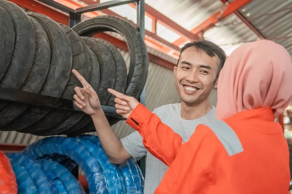 아시아의 남성 소비자는 타이어를 보면서 베일을 쓴 여성 정비공이 있는 타이어를 손가락으로 선택 한다 — 스톡 사진