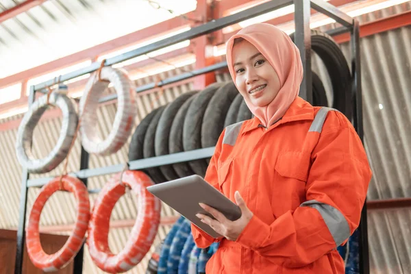 veiled female mechanic looks at the camera while using a digital tablet standing