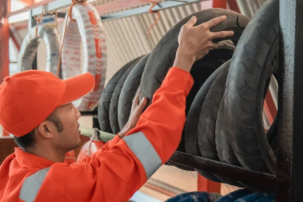 Mecánico en un uniforme de wearpack recoge un neumático de la rejilla —  Fotos de Stock