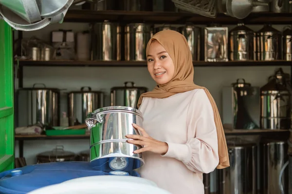 Hijab vendedor feminino sorrindo quando olhar para a câmera enquanto segurando a panela — Fotografia de Stock