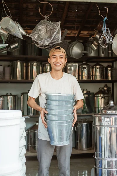 Vendedor masculino sorrindo enquanto carrega lotes de baldes — Fotografia de Stock