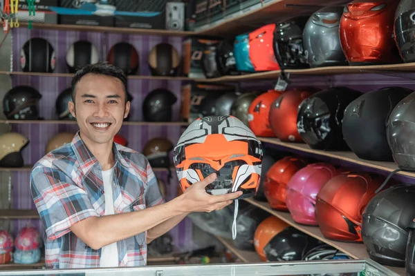 亚洲男性售货员一边拿着头盔一边用手势笑着提供一些东西 — 图库照片