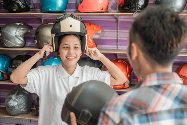 Giovani donne scelgono un casco e indossarlo quando servito da un assistente di negozio — Foto Stock