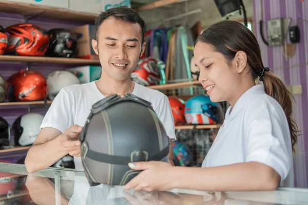 Asistentes de tienda masculinos y femeninos sosteniendo un casco contra un fondo de estante de exhibición de casco —  Fotos de Stock