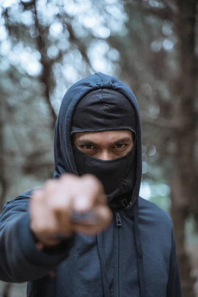 Gemaskerde man met een mes in zwarte kleren met dreigende ogen — Stockfoto