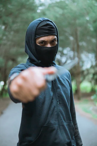 Close-up van de dief in een masker dragen zwarte hoodie gericht het mes op de camera — Stockfoto