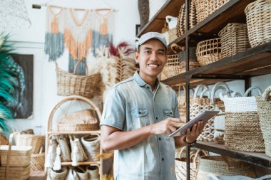 Gülümseyen genç girişimci elinde dijital tabletle kameraya bakıyor.