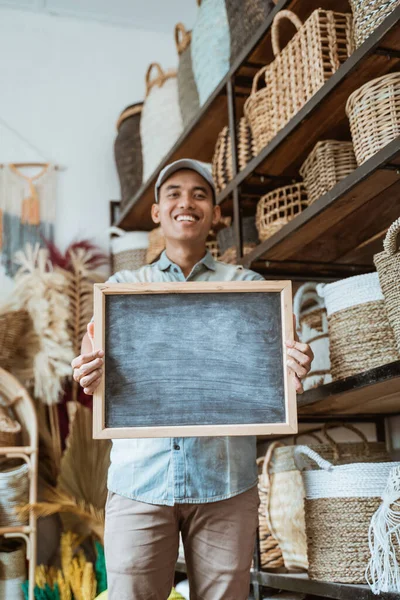Lächelnder Mann blickt in die Kamera und hält eine Tafel in einer Bastelwerkstatt — Stockfoto