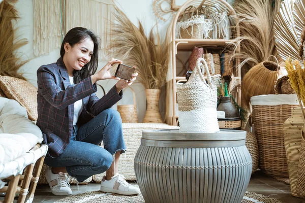 Vrouw in blazer met behulp van een camera smartphone bij het nemen van een geweven tas geschoten in een handwerk winkel — Stockfoto