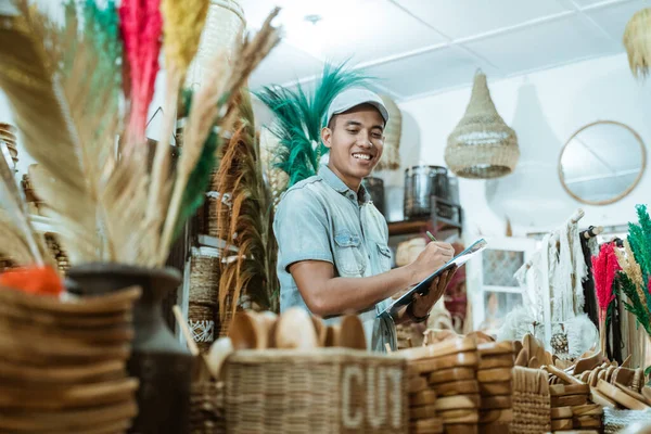 Smiling man holds the clipboard while list items among craft items — Stock Photo, Image