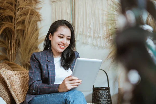 Uma mulher de carreira em um blazer usa um tablet digital enquanto sentado casualmente — Fotografia de Stock