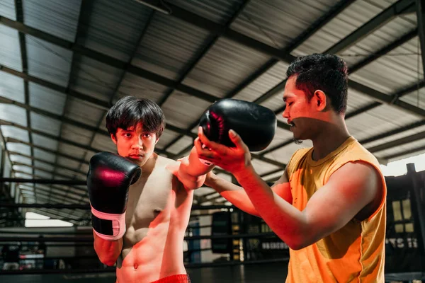 Мужчина в боксёрских перчатках с тренером, делающим ударные упражнения на боксерском ринге — стоковое фото