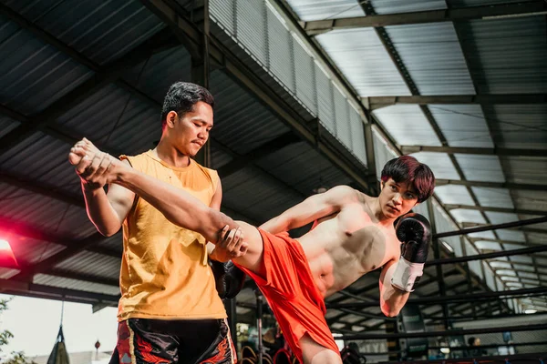 Pria berotot tinju dalam sarung tangan dengan pelatihnya melakukan latihan menendang pada ring tinju — Stok Foto