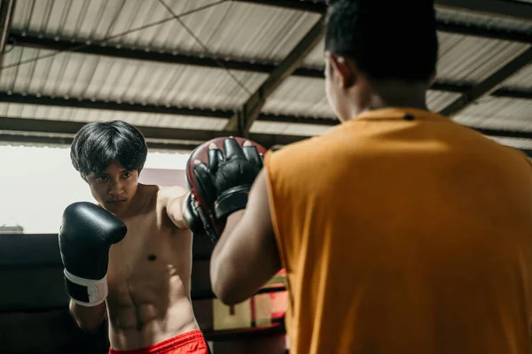 Boxeador júnior e treinador de treinamento, juntamente com almofadas de perfuração no ringue de boxe — Fotografia de Stock