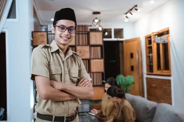 Professor masculino em uniforme de funcionário público sorrindo com uma mão cruzada enquanto trabalhava com a equipe de casa — Fotografia de Stock