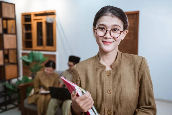 Жінка-вчителька в уніформі державного службовця в окулярах посміхається під час носіння книги — стокове фото
