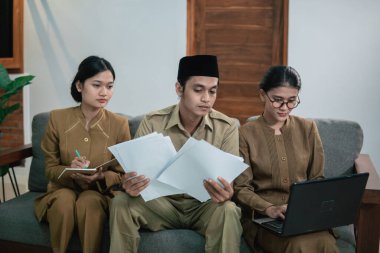 Elinde gazete tutan ciddi bir devlet memuru ve devlet memuru üniforması giyen iki kadın asistan.