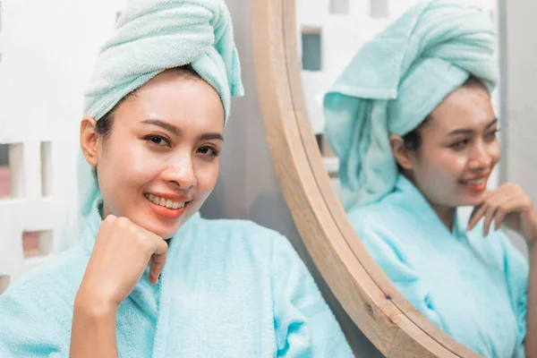 Γυναίκα χαμογελά βλέποντας την κάμερα στέκεται δίπλα στον καθρέφτη με ένα άγγιγμα του καθαρού δέρματος — Φωτογραφία Αρχείου