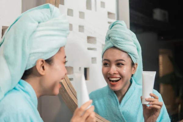 Mulher sorrindo usando toalha segurando tubo de espuma facial para nutrição pele saudável — Fotografia de Stock