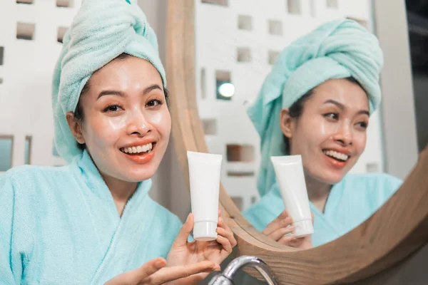 Jovem mulher asiática segurando pele cuidado creme tubo com rosto sorridente — Fotografia de Stock