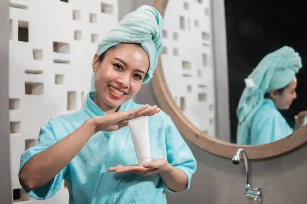 Bela ásia jovem mulher rosto segurando e apresentando creme tubo produto — Fotografia de Stock