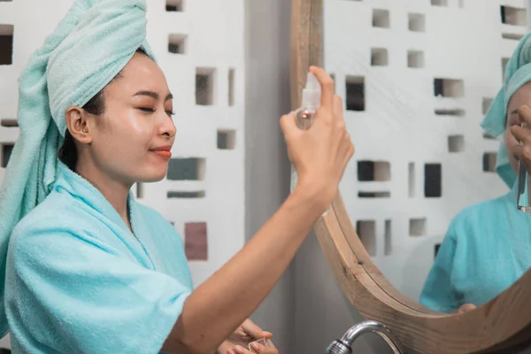 Азиатка носит полотенце, распыляя увлажняющий крем для кожи лица — стоковое фото