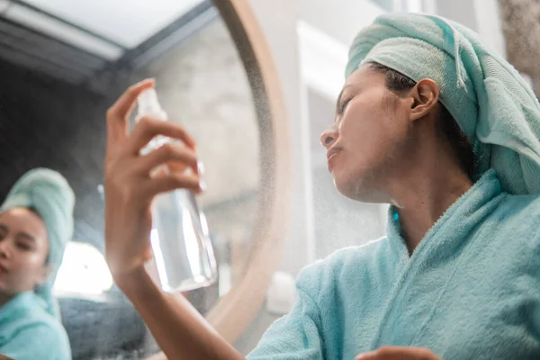 Las mujeres usan una toalla al rociar humectante de la piel facial con una botella de aerosol —  Fotos de Stock