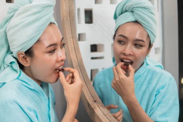 Счастливая азиатская женщина с полотенцем едят таблетки с витамином Е для питания здоровой кожи — стоковое фото
