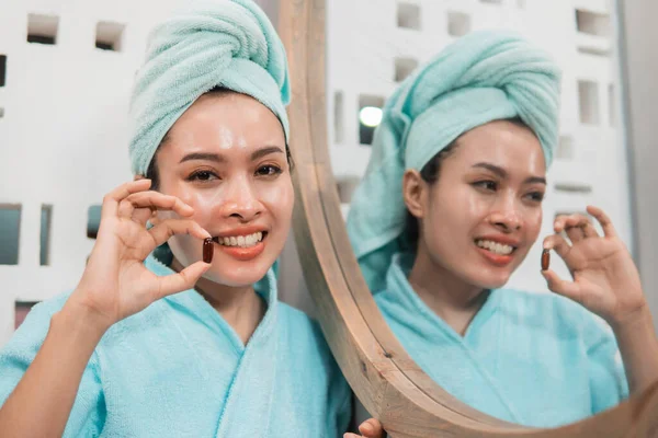 Uśmiechnięta kobieta nosząca ręcznik biorąc pigułkę z witaminą E dla odżywiania zdrowej skóry — Zdjęcie stockowe