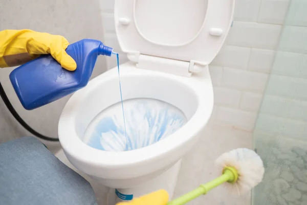 Jemand mit einem Handschuh schüttete die Reinigungsflüssigkeit aus und hielt die Bürste während der Toilettenreinigung — Stockfoto