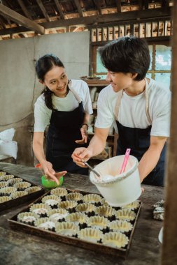 Pasta tepsisine hamur dökerken önlük takan gülümseyen çift birbirlerine bakıyorlar.